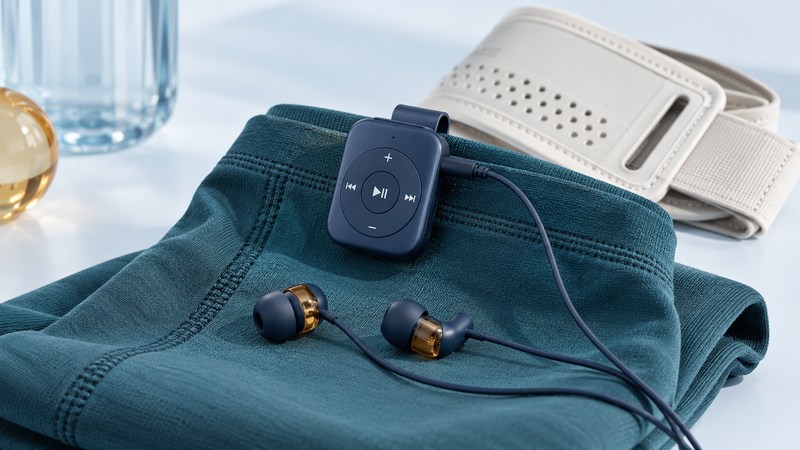 A navy clip-on music player attached to teal fabric beside wired earbuds and an armband.